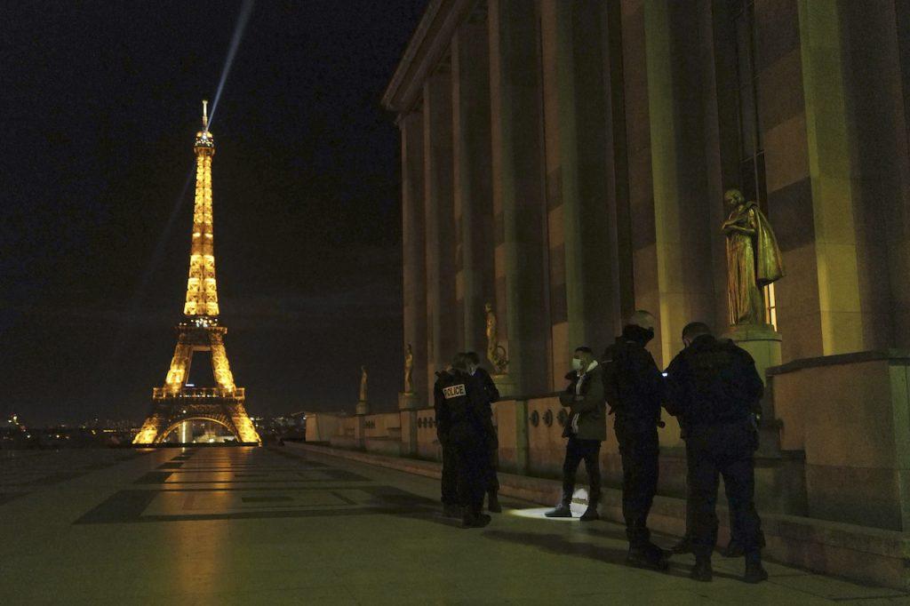 French police officers stop a person near the Eiffel Tower as they enforce a curfew in Paris, Dec 15. Top health advisers say a third lockdown will probably be needed soon to combat the spread of infections in France. Photo: AP