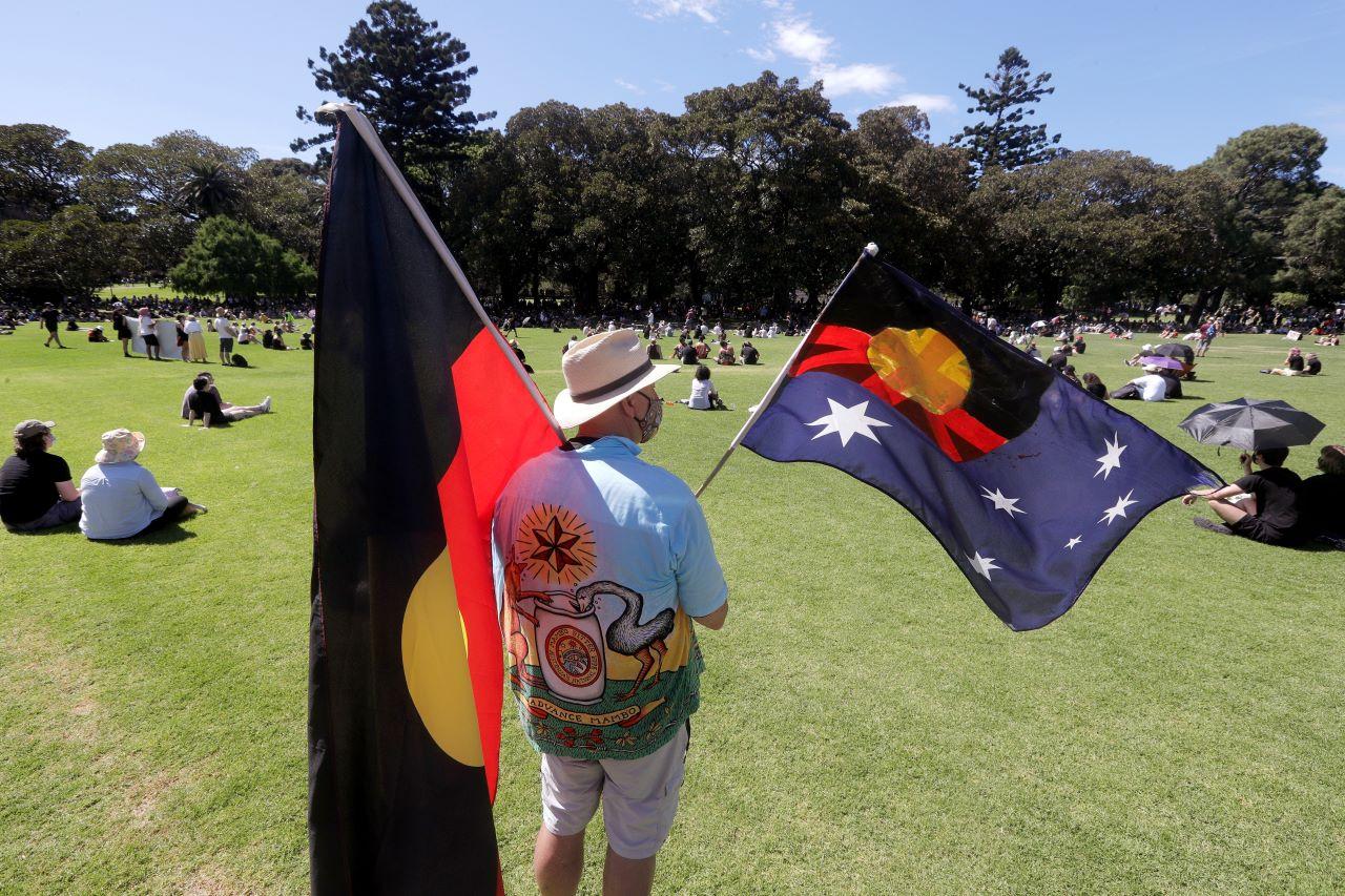 A man holds a modified Australian flag and the Aboriginal flag in a social distanced crowd during an Aboriginal-lead Invasion Day rally on Australia Day in Sydney, Jan 26. Many of Australia's First Nations people say that sovereignty has never been ceded and oppose ongoing colonial violence and destruction. Photo: AP