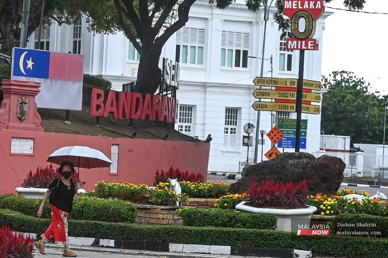 Seorang wanita melintas jalan sambil berpayung dan memakai pelitup muka di bulatan Pusat Bandar Melaka.