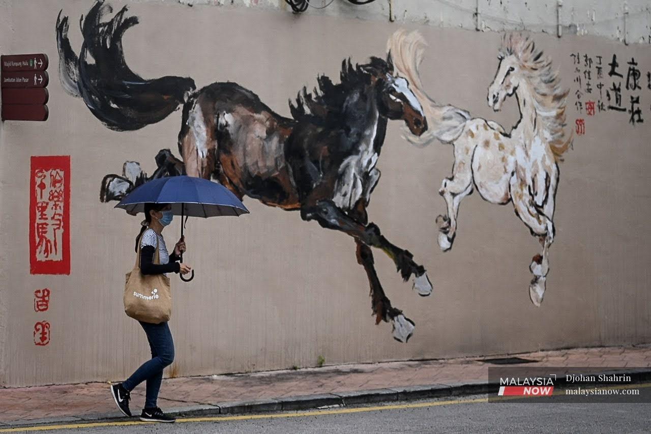 Seorang wanita melalui kawasan Jonker Street, Melaka berlatarbelakangkan mural dua ekor kuda.
