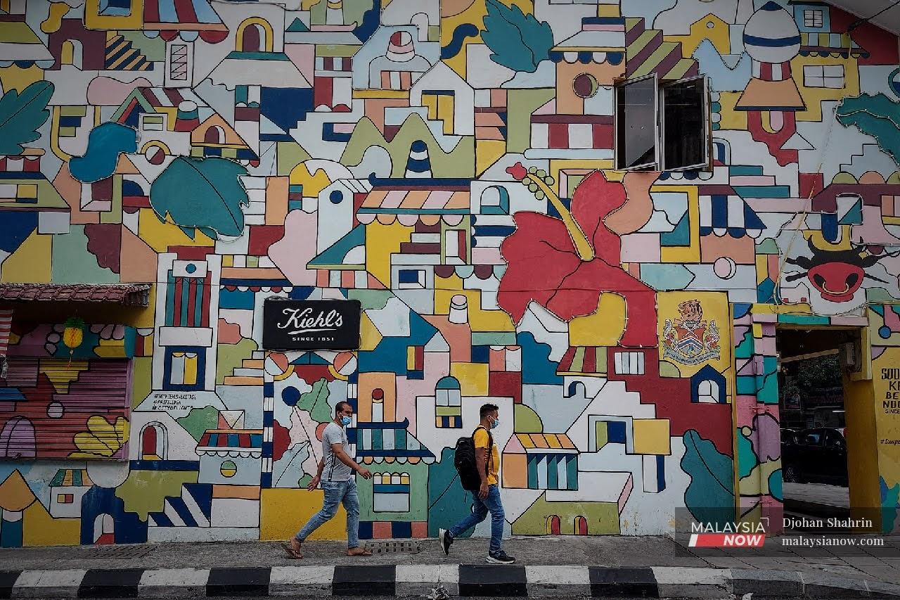 Dua orang pejalan kaki melalui kawasan lukisan mural yang terdapat pada dinding bangunan kedai di Jalan Tun H.S Lee, Kuala Lumpur.