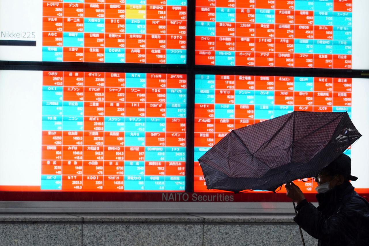 A man wearing a protective mask tries to open an umbrella in front of an electronic stock board showing Japan's Nikkei 225 index at a securities firm in Tokyo, Feb 15. Photo: AP
