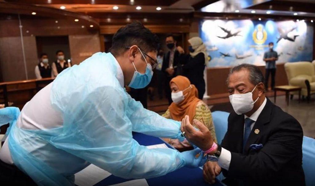 A health ministry officer puts a wristband on Prime Minister Muhyiddin Yassin upon his return from Jakarta, indicating that he is under quarantine.