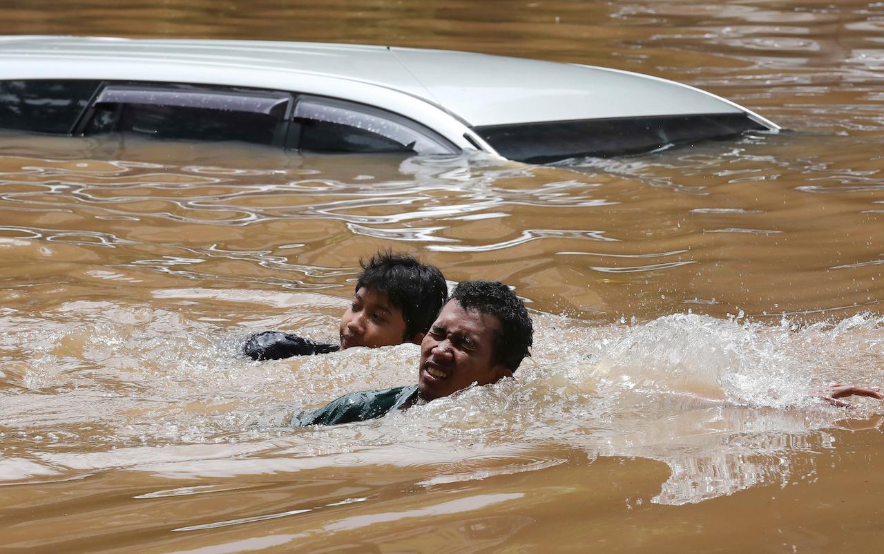 People swim through a flooded neighborhood following heavy rains in Jakarta, Indonesia, Feb 20. Photo: AP
