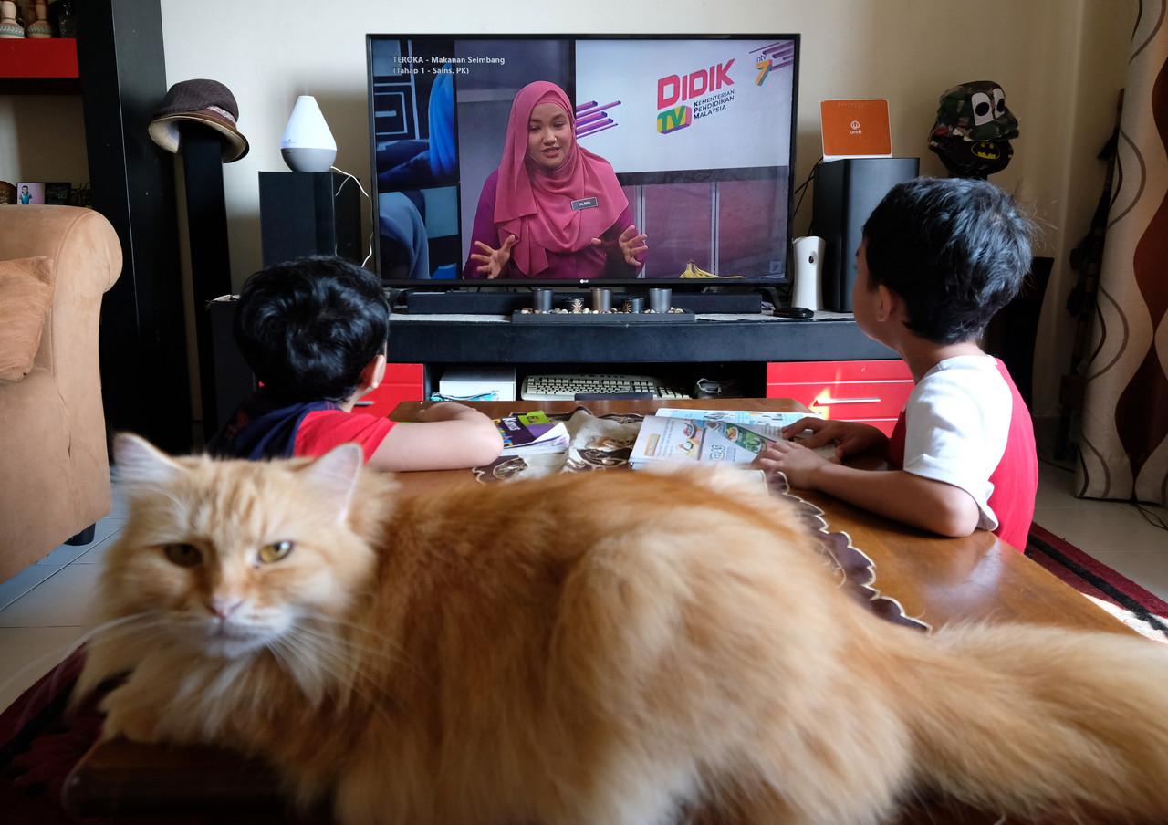 A cat keeps a stern eye as two brothers watch a teacher speaking on the DidikTV educational TV channel, used to help facilitate home-based learning during the pandemic season which has kept many students away from physical classrooms for months. Educationists say correcting those who are not fluent in English should be done in a constructive manner, after a teacher was criticised for poor pronunciation. Photo: Bernama