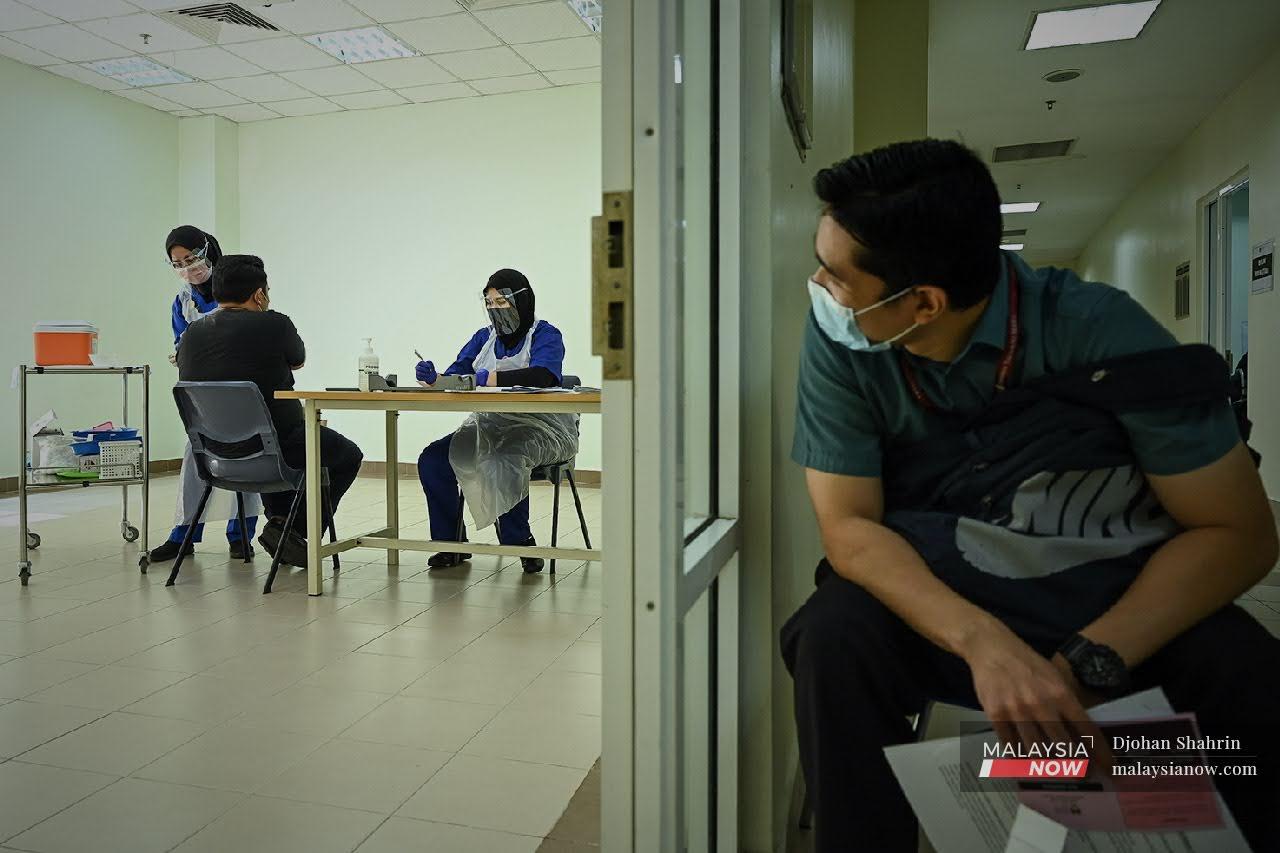 A frontline worker waiting for his turn to be vaccinated peeks through the door at a colleague receiving his Covid-19 jab under Phase 1 of the national inoculation programme at Hospital UiTM in Sungai Buloh today.