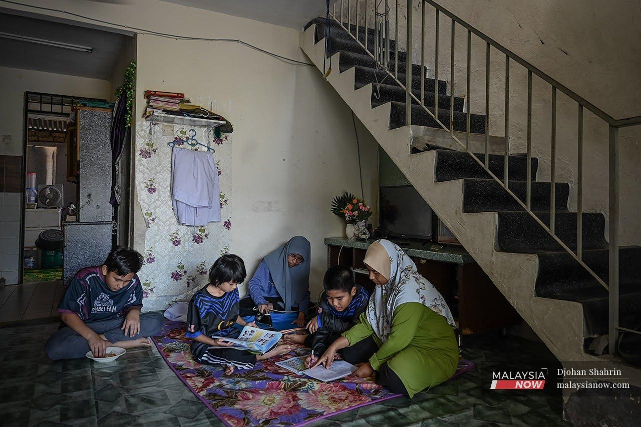Seated on a rug in the corner of her house, Norhanita Abdul Halim checks the activity books of her children who will return to school on March 8. Hers is among the many families in the B40 category who are struggling to follow home-based learning as well as to equip their children with school supplies and uniforms for face-to-face classes.