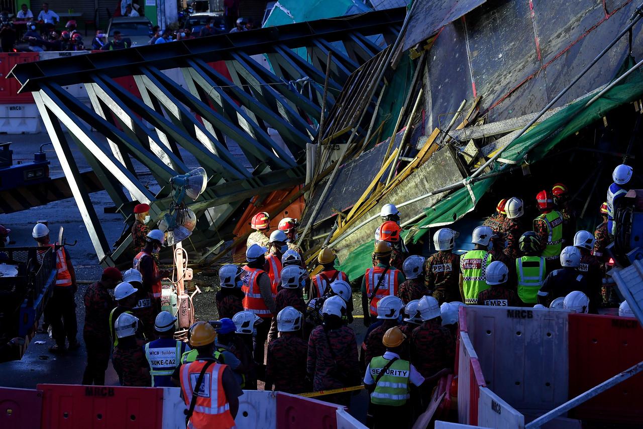 Members of the Fire and Rescue Department work to recover a victim trapped beneath the rubble of an overhead bridge structure which collapsed last night after a trailer crashed into the iron scaffolding. Photo: Bernama