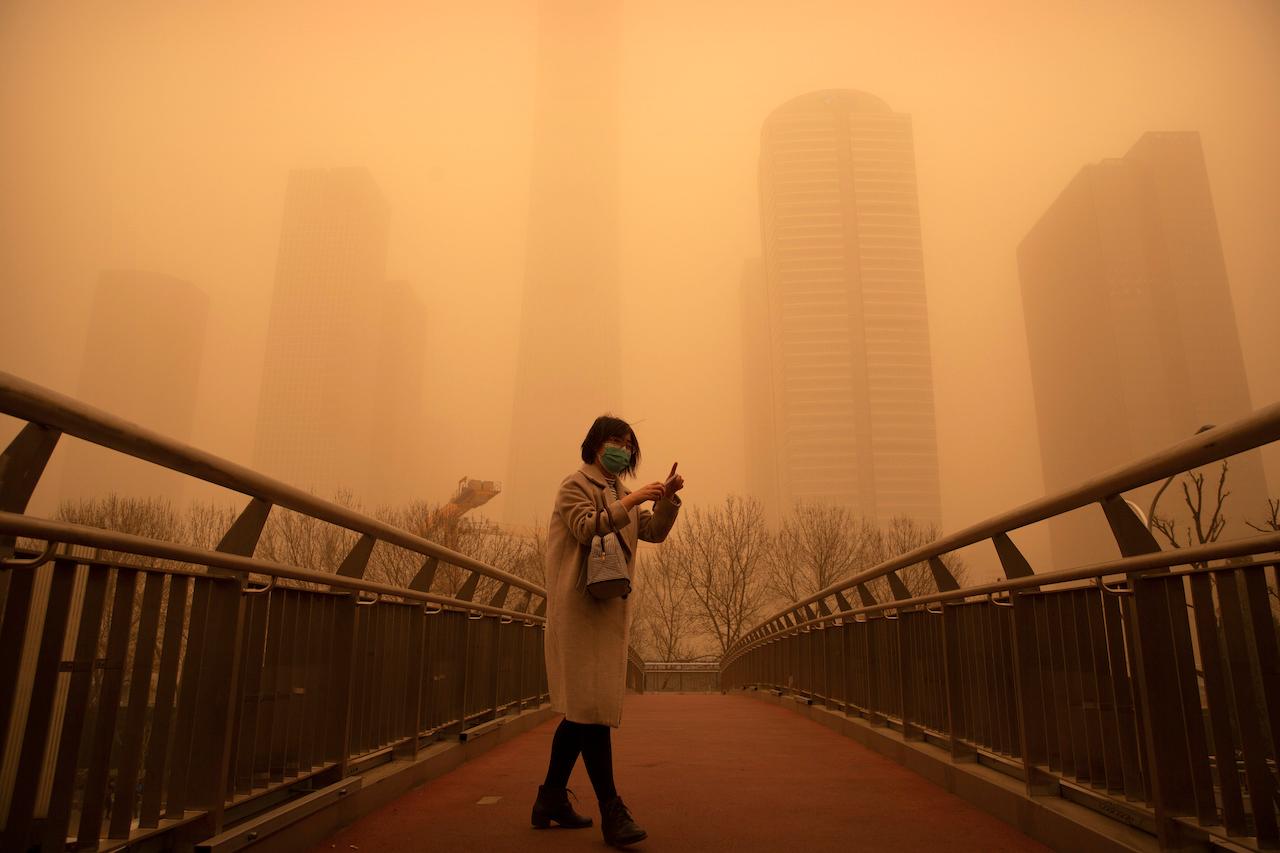 A woman walks along a pedestrian bridge amid a sandstorm during the morning rush hour in the central business district in Beijing, March 15. The sandstorm brought a tinted haze to Beijing's skies and sent air quality indices soaring on Monday. Photo: AP