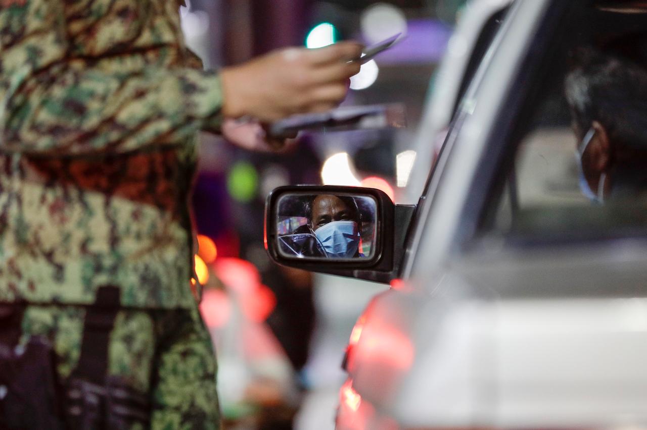 A man watches from his car as police inspect his identification cards at a checkpoint as curfew is imposed to prevent the spread of the coronavirus in Metro Manila, Philippines, a year after the country imposed a lockdown, March 15. Photo: AP