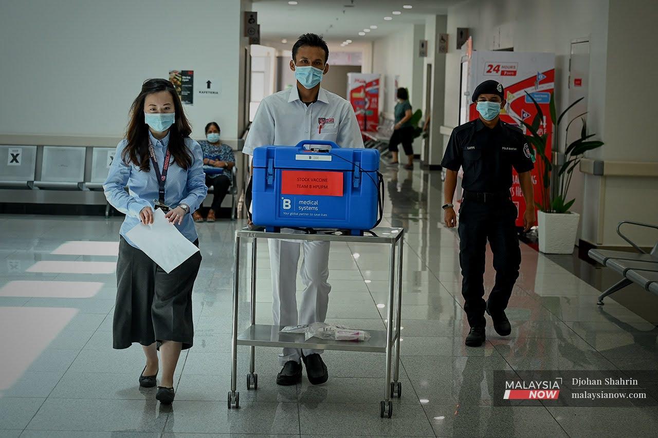 A pharmacist accompanies another staff member wheeling a batch of Pfizer-BioNTech vaccine in a temperature-controlled box to the vaccine administration room under police escort at Hospital Pengajar Universiti Putra Malaysia.
