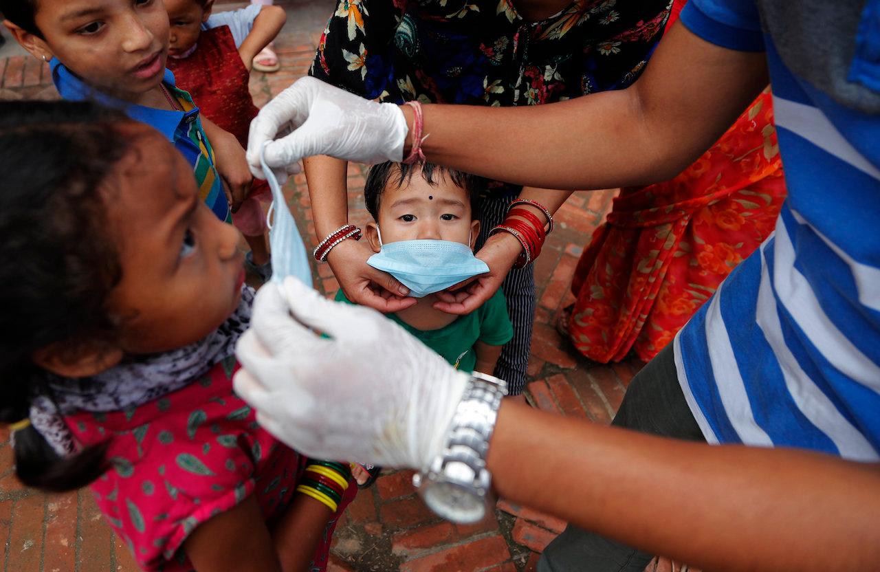A volunteer hands out free face masks to children in Lalitpur, Nepal. Side effects of Covid-19 lockdowns in the country include an 80% drop in the number of young children treated for severe acute malnutrition, a new UN report says. Photo: AP