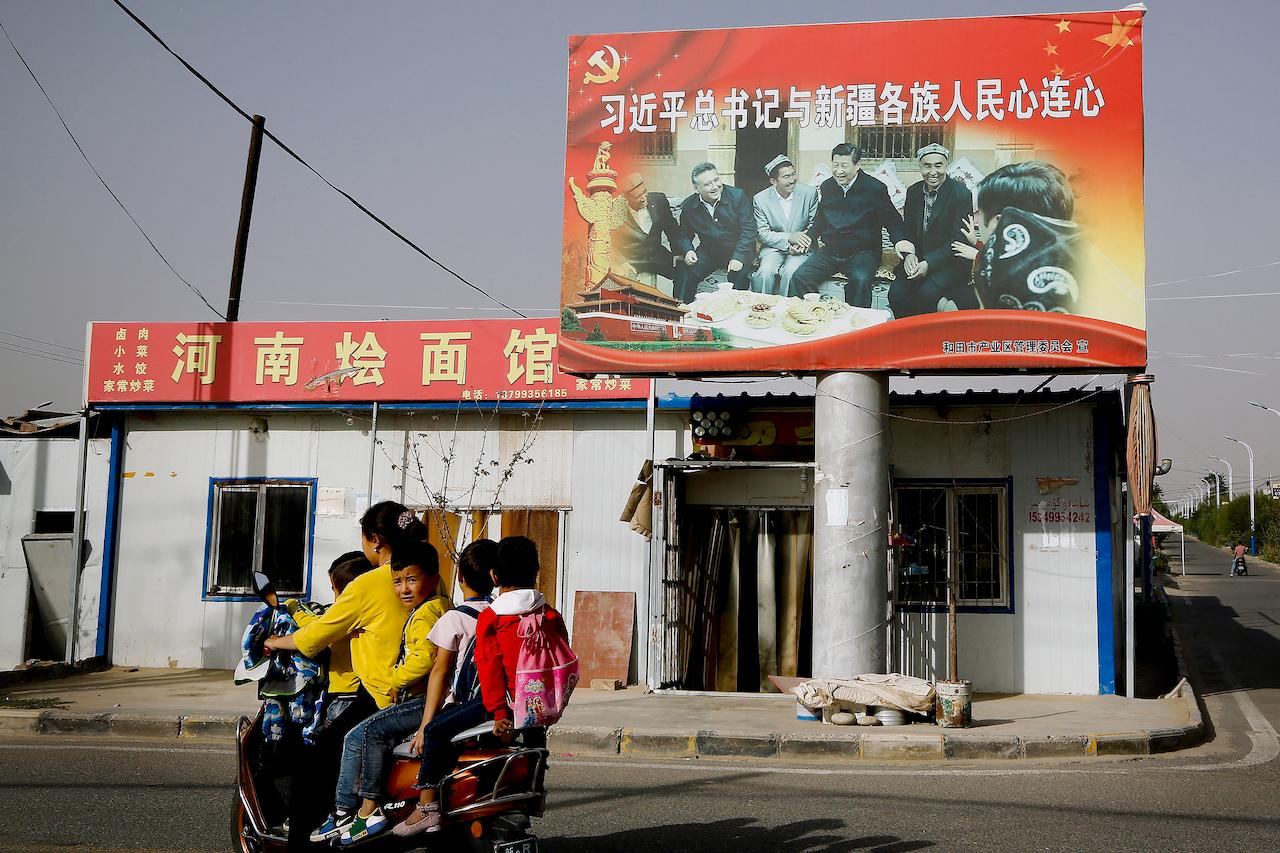 In this Sept 20, 2018, file photo, an Uighur woman uses an electric-powered scooter to fetch school children as they ride past a picture showing China's President Xi Jinping joining hands with a group of Uighur elders at the Unity New Village in Hotan, in western China's Xinjiang region. Photo: AP