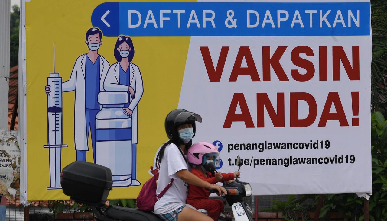 A woman and a child on a motorcycle ride by a billboard urging members of the public to register for Covid-19 vaccination in Jalan Air Itam, George Town, Penang. Photo: Bernama