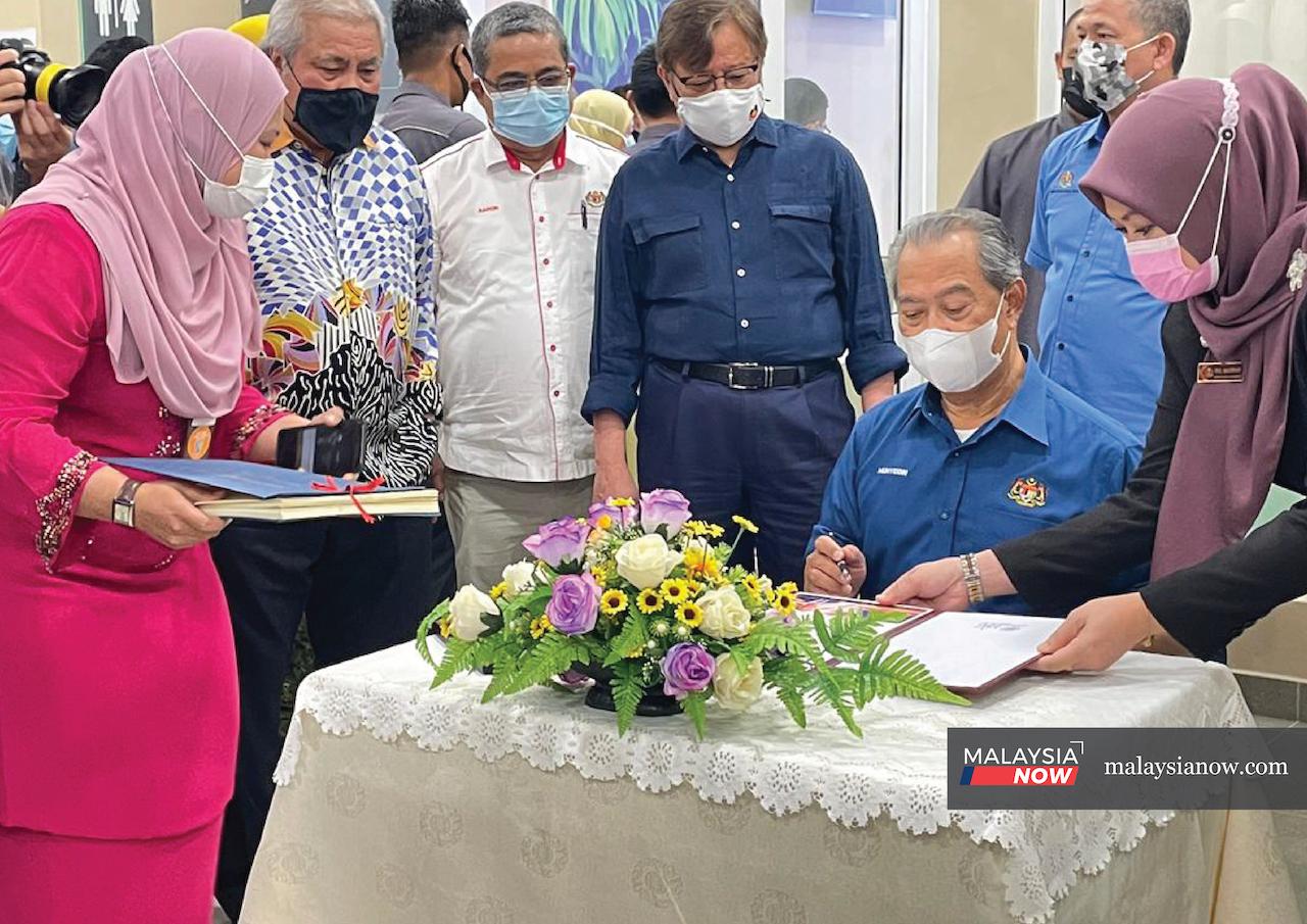 Prime Minister Muhyiddin Yassin (seated) signs the guest book during a visit to the Sarawak General Hospital in Kuching today. Accompanying him is Chief Minister Abang Johari Openg (standing, left).