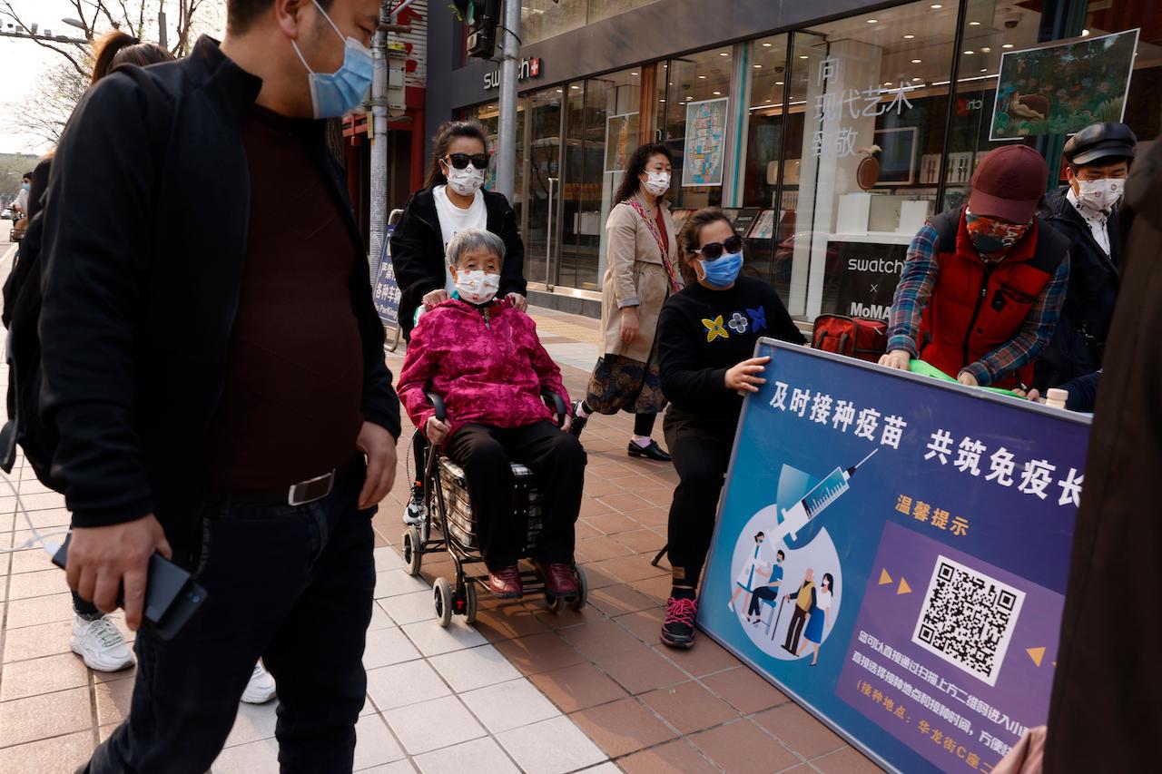 A woman in a wheelchair is pushed past a stand promoting Chinese coronavirus vaccines in Beijing, April 9. In a rare admission of the weakness of Chinese coronavirus vaccines, the country's top disease control official says their effectiveness is low and the government is considering mixing them to give them a boost. Photo: AP
