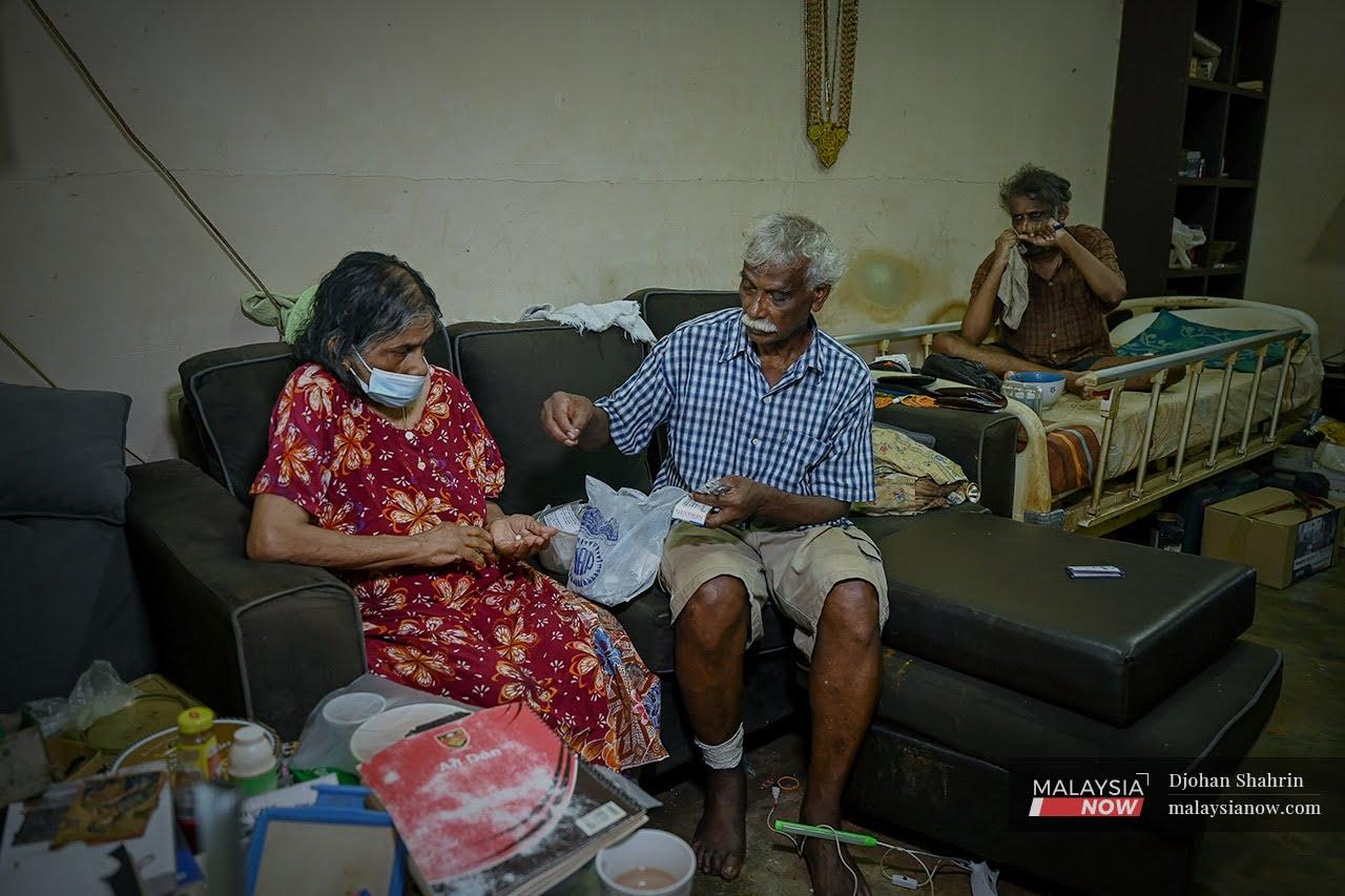 A Arullapan counts out the day's pills for his wife, Annamary Sokkan, who suffered a stroke six years ago, while their son Pius sits nearby on a bed set up in the living room.