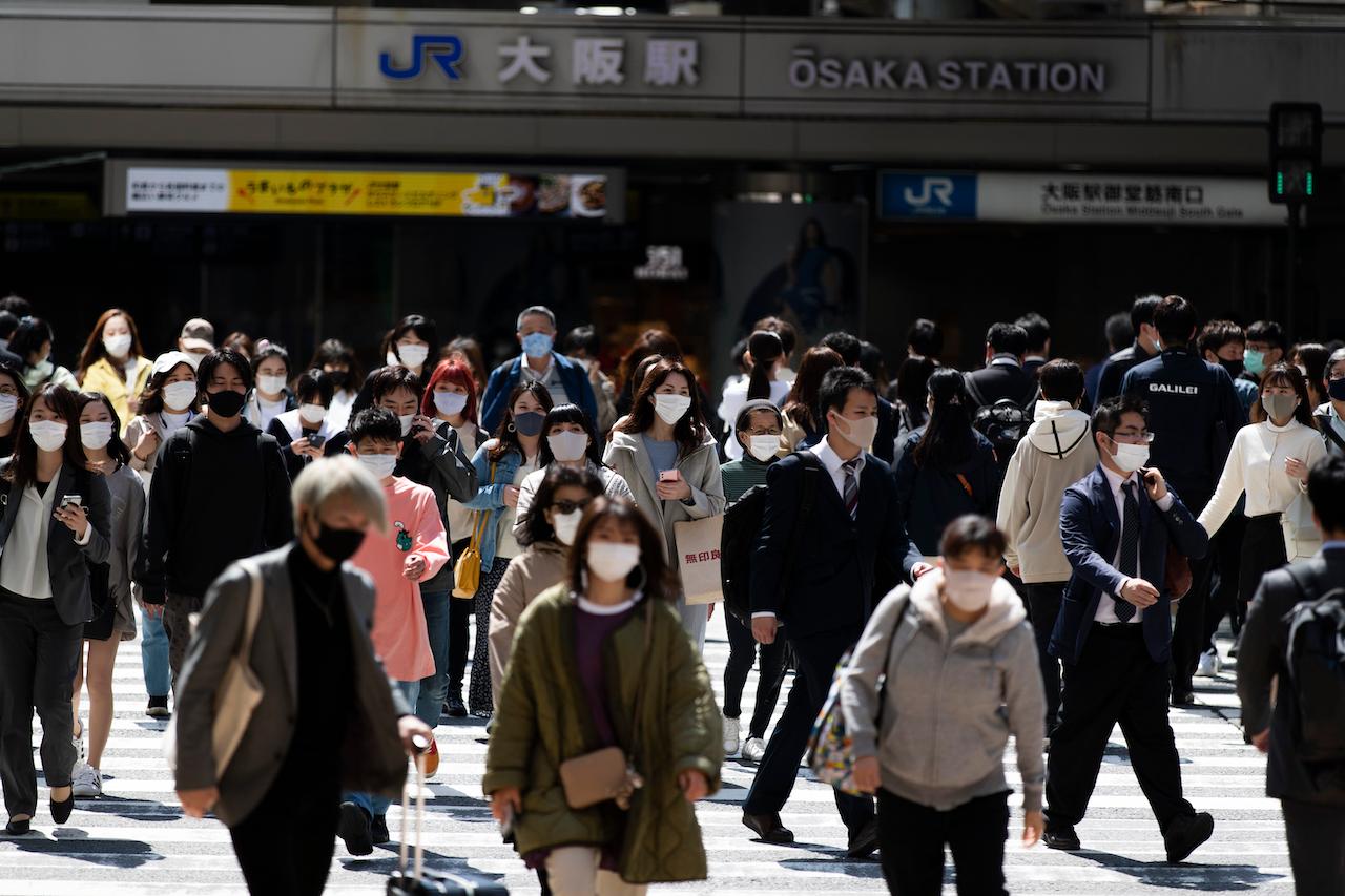 People wearing face masks walk across an intersection by the Osaka train station in Osaka, western Japan, April 19. Japan this month put Osaka, Tokyo, and eight other prefectures under 'quasi-states of emergency' aimed at controlling the spread of Covid-19. Photo: AP