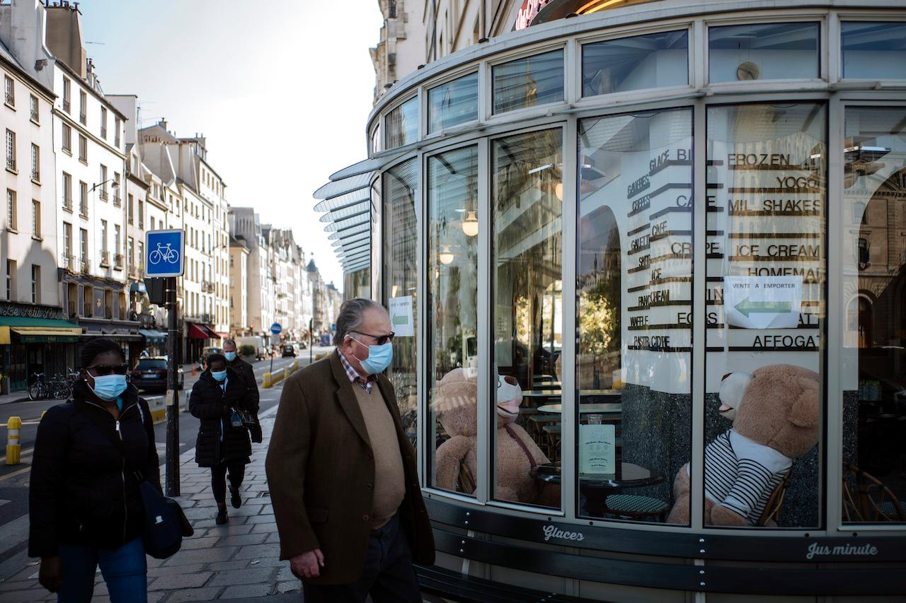 People wearing face masks to prevent the spread of Covid-19 walk past a closed restaurant with teddy bears inside, in Paris, April 19. Businesses deemed to be 'non-essential' have been forced to close since the beginning of the month in France. Photo: AP