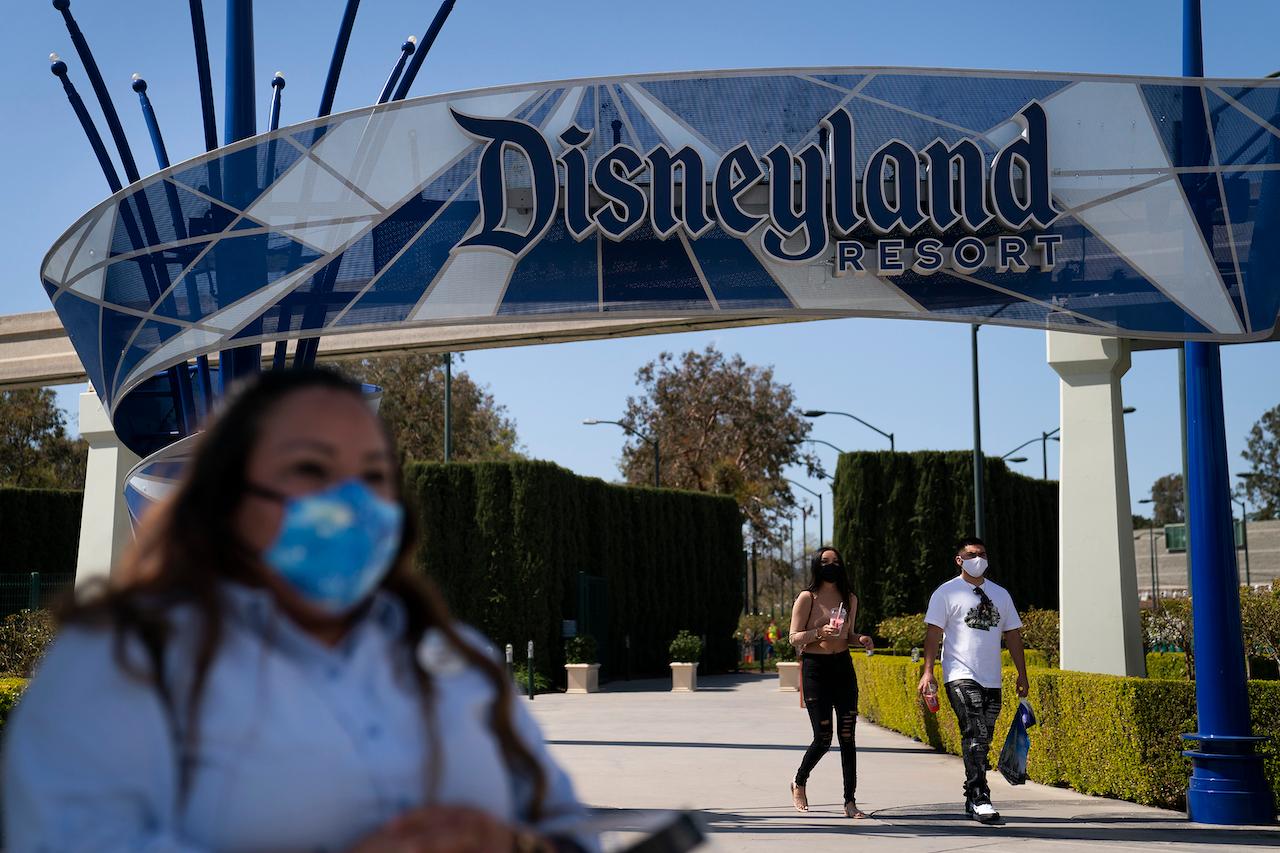 In this March 9 file photo, a woman wearing a face mask waits to cross the street outside Disneyland Resort in Anaheim, California. Disneyland Park and Disney California Adventure Park will reopen to visitors April 30. Photo: AP