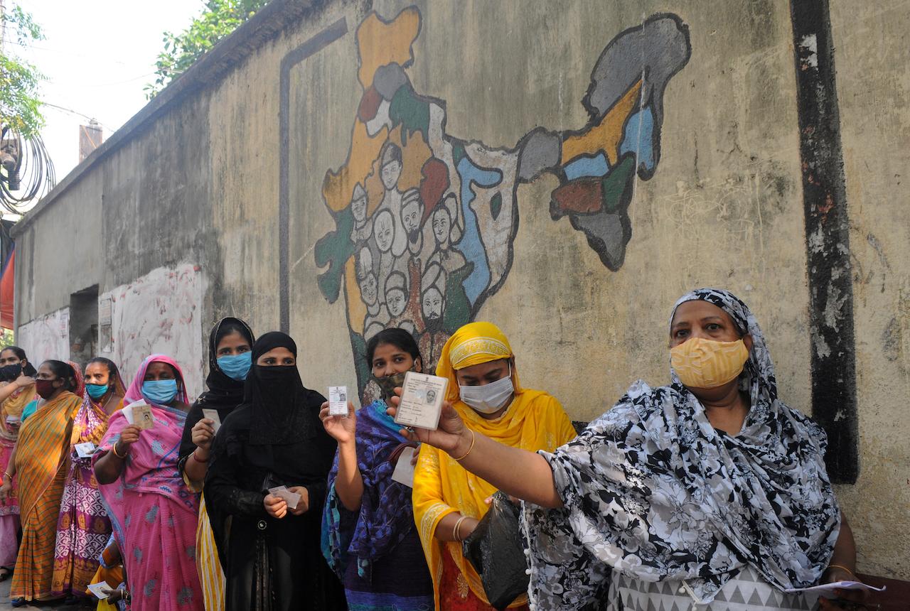 Indian women wearing face masks as a precaution against the coronavirus display identity cards as they wait to cast their votes at a polling station during the last phase of West Bengal state elections in Kolkata, India, April 29. Photo: AP