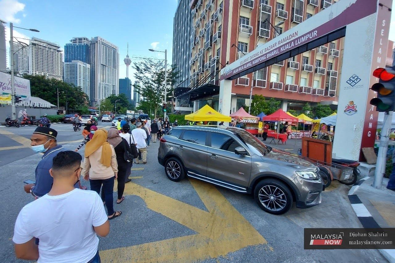Orang ramai beratur panjang menunggu giliran untuk masuk ke bazar Ramadan di Kuala Lumpur. Peningkatan kes dalam negeri menyebabkan kerajaan mempertimbangkan pelaksanaan sekatan yang lebih ketat demi membendung Covid-19.