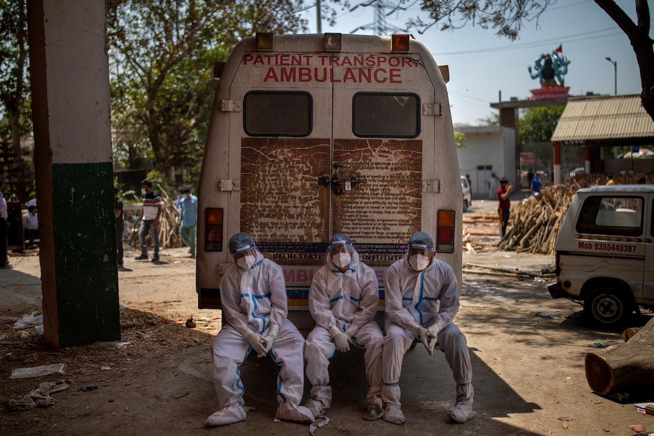 In this April 24 file photo, exhausted workers who carry the dead for cremation sit on the rear step of an ambulance in New Delhi, India. Photo: AP
