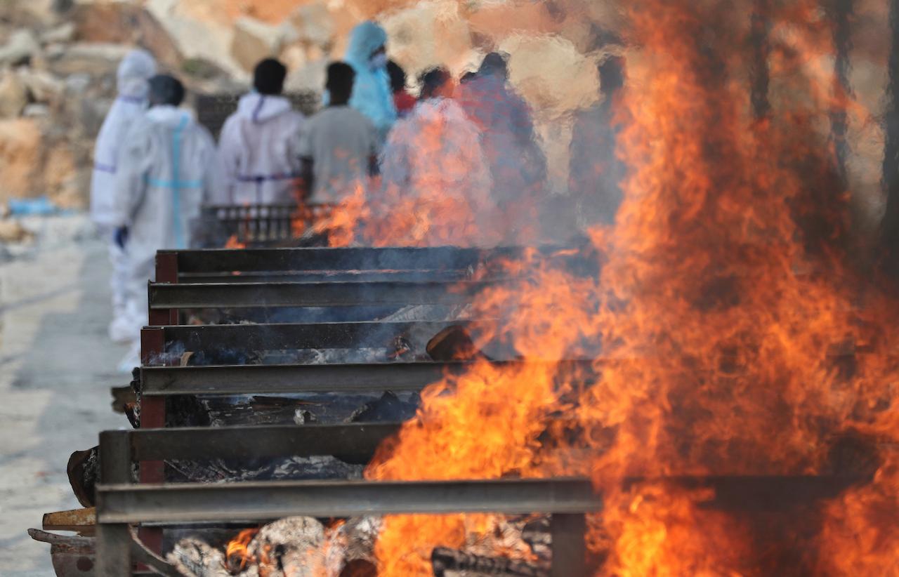 Family members perform last rites of a person who died of Covid-19 as funeral pyres of other victims burn at an open crematorium set up at a granite quarry on the outskirts of Bengaluru, India, May 5. Photo: AP