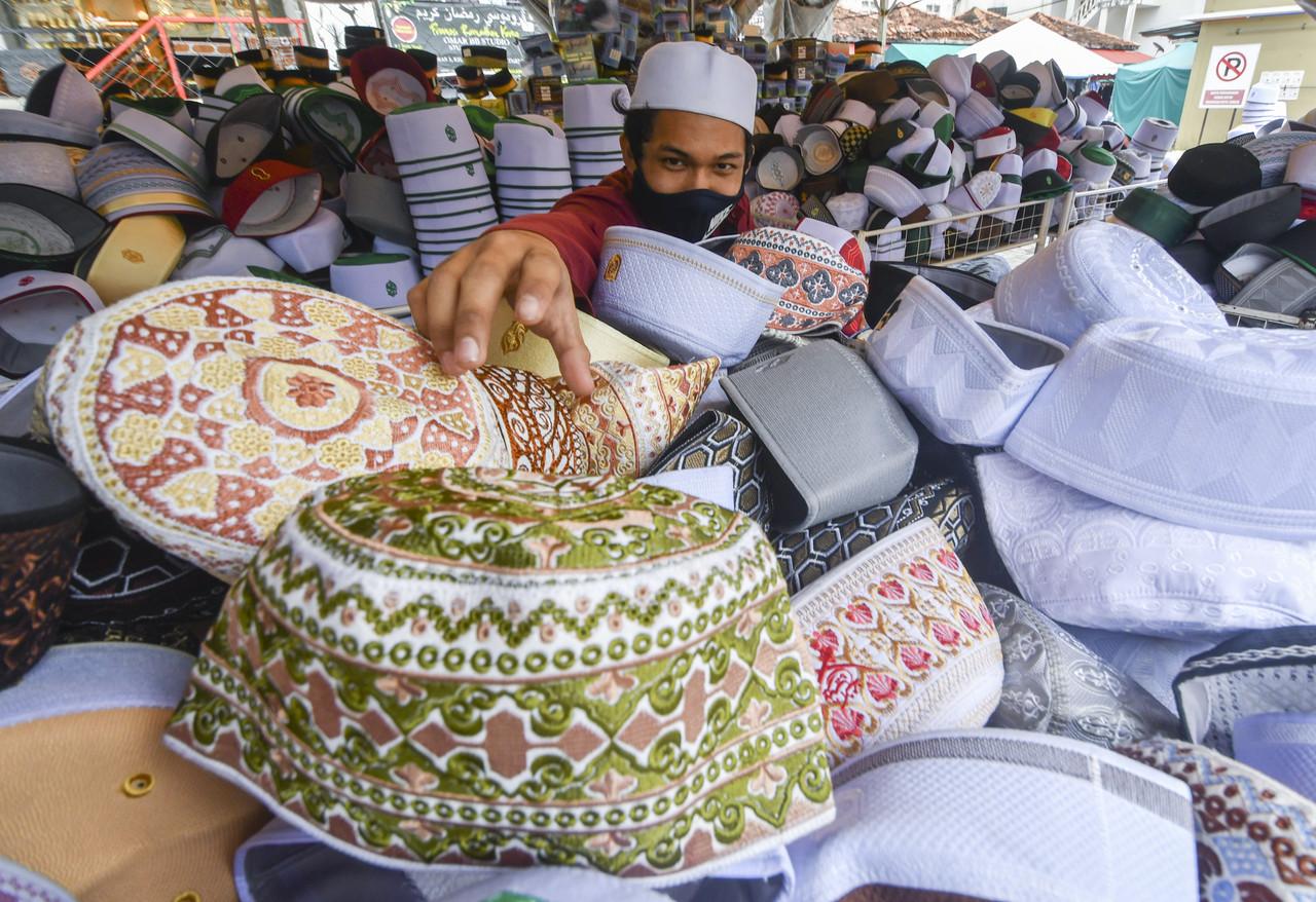 Pembantu kedai, Muhamad Danial Che Mohd Khairul Hazian, 18, memeriksa sebahagian kopiah yang dijual sebagai persediaan jualan menjelang Aidilfitri ketika tinjauan di hadapan Masjid Muhammadi di Kota Bharu, Kelantan pada 29 April, 2021. Gambar: Bernama