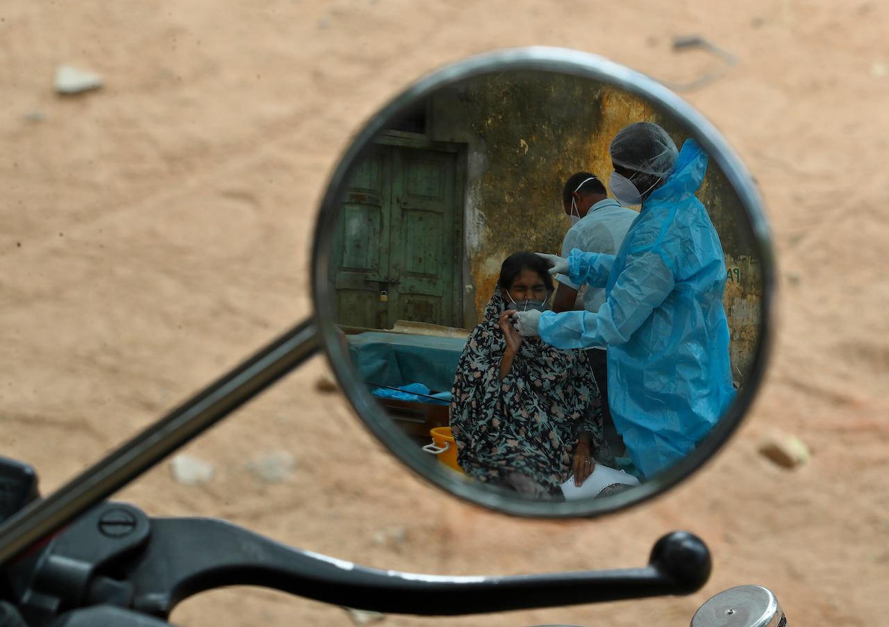 A health worker reflected in the mirror of a motorcycle takes a nasal swab sample from a woman to test for Covid-19, in Hyderabad, India, May 7. Photo: AP