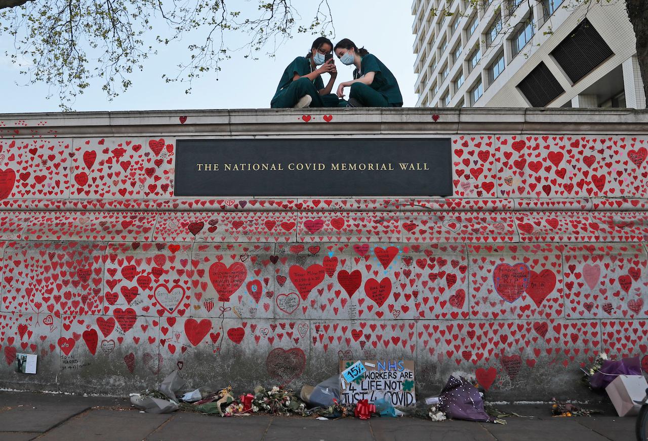 Nurses from the nearby St Thomas' hospital sit atop the National Covid Memorial Wall in London, April 27. Around 53% of the British population have received one dose of vaccine while more than a quarter have had two jabs – one of the speediest vaccine rollouts in the world. Photo: AP