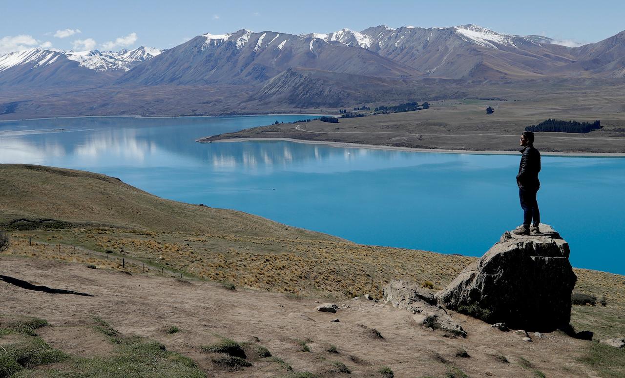 A tourist stands on a rock as he looks over Lake Tekapo and the Southern Alps in New Zealand, Oct 6, 2018. Photo: AP