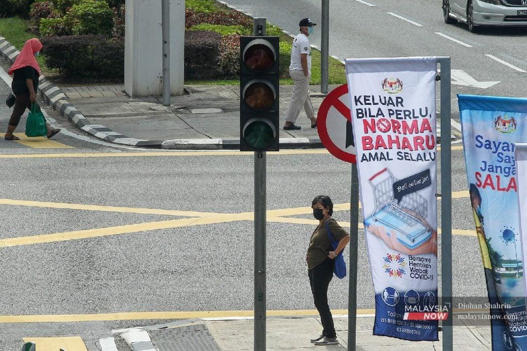 A woman stands near a sign on a street corner in Kuala Lumpur, urging the public to be mindful of SOPs under the new norm.