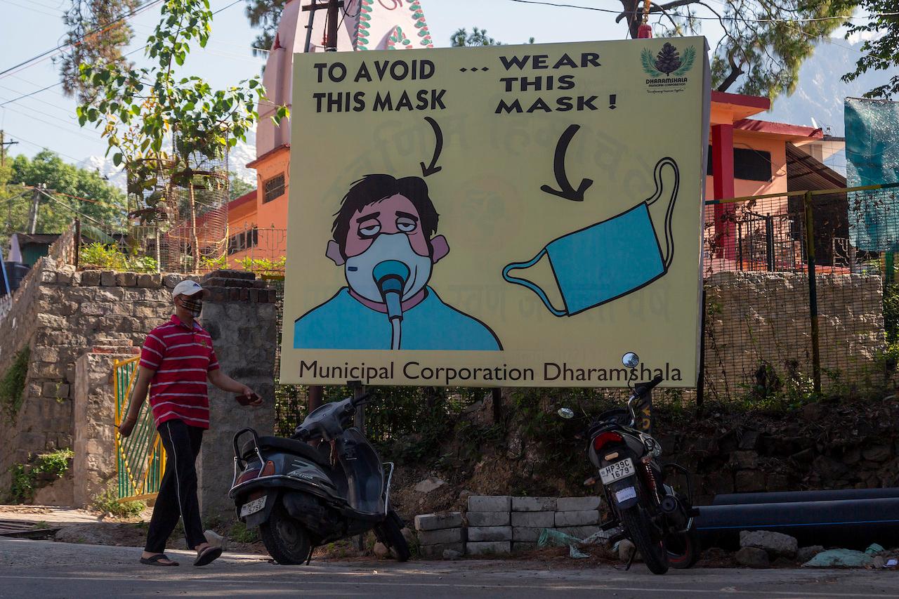 A man walks past a billboard warning people to wear masks during a relaxation in curfew imposed to curb the spread of the coronavirus in Dharmsala, India, May 17. Photo: AP