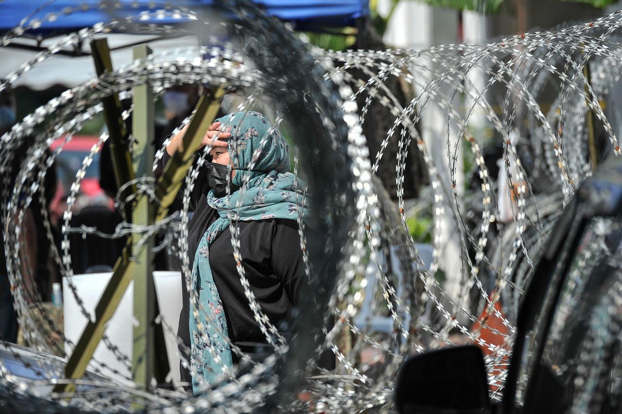 A resident at the Kampung Limau People's Housing Project in Kuala Lumpur walks behind a barbed wire fence, put up after the area was placed under enhanced movement control order yesterday. Photo: Bernama