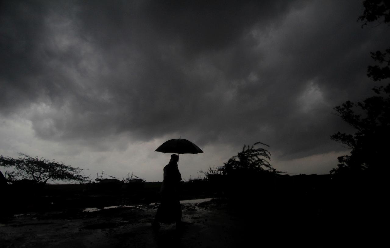 A villager walks holding an umbrella as dark clouds loom over during a drizzle in Balasore district in Odisha, India, May 25. Tens of thousands of people were evacuated in low-lying areas of two Indian states and moved to cyclone shelters to escape a powerful storm barreling toward the eastern coast. Photo: AP