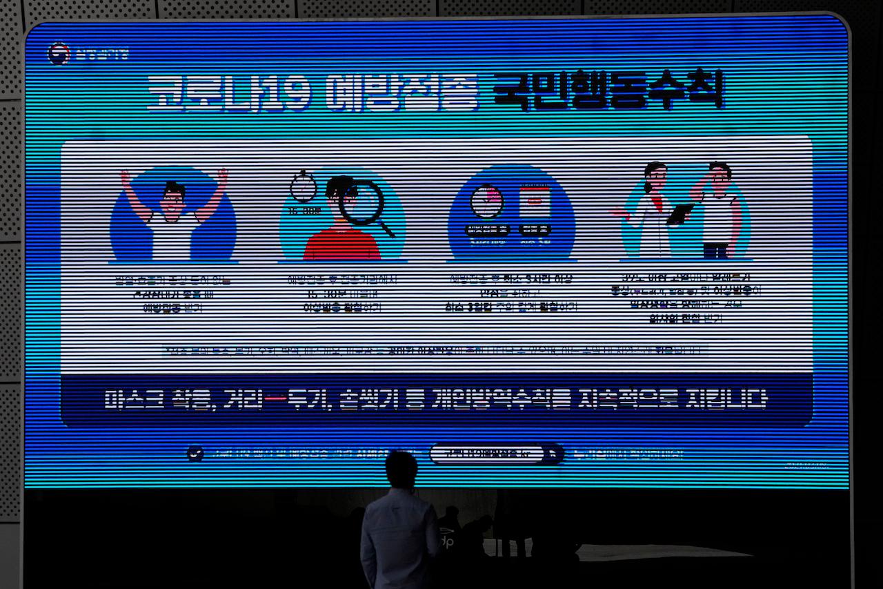 A man wearing a face mask looks at a screen displaying precautions against the coronavirus in Seoul, South Korea, May 24. The letters read 'Keep social distancing and mandatory mask wearing as a prevent the spread of the coronavirus.' Photo: AP