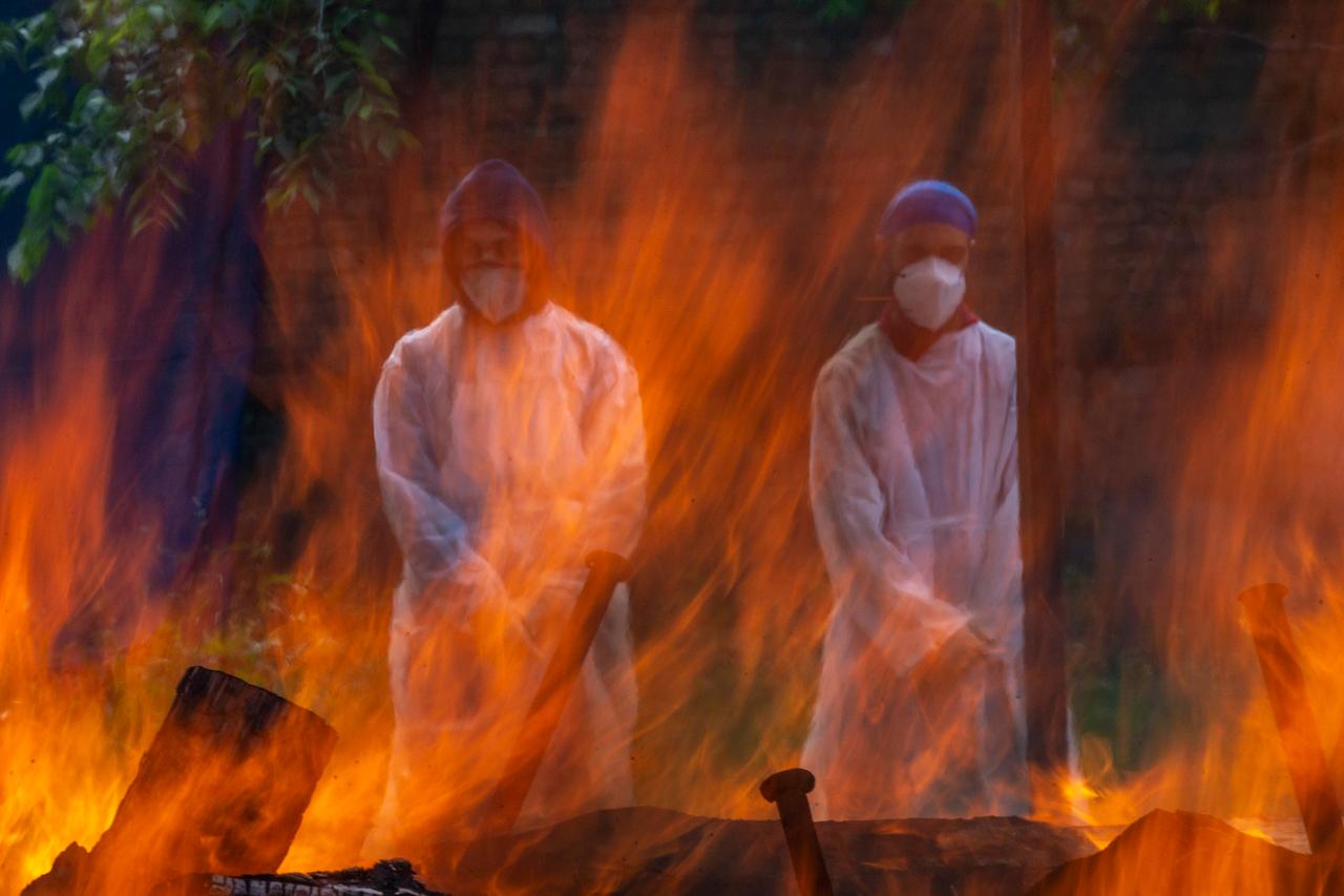 Relatives in protective suits stand next to the burning pyre of a person who died of Covid-19, at a crematorium in Srinagar, Indian-controlled Kashmir, May 25. Photo: AP