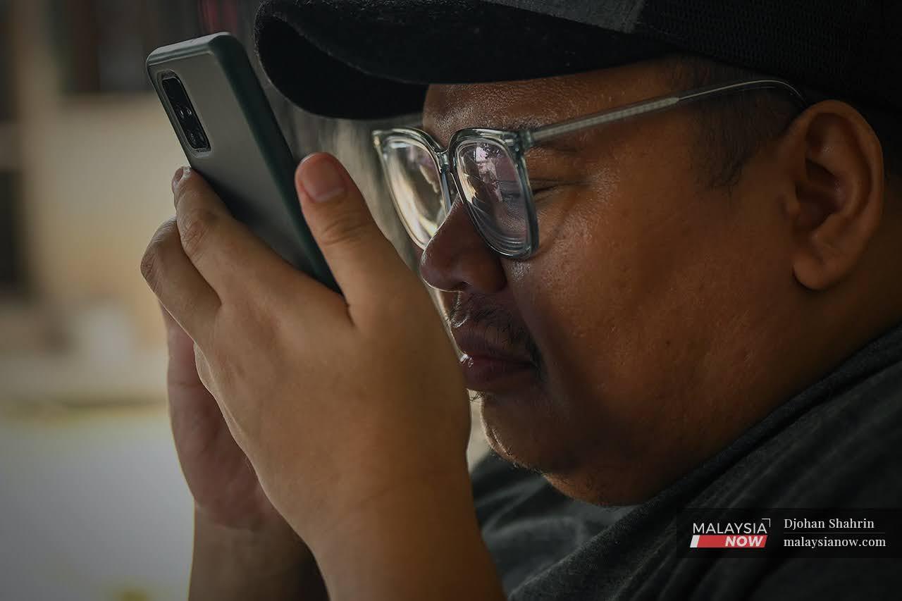 Mohd Kamil Affendy Hashim peers at the screen of his phone. His eyesight has been on the decline, causing him to lose his job as a taxi driver in the city centre.
