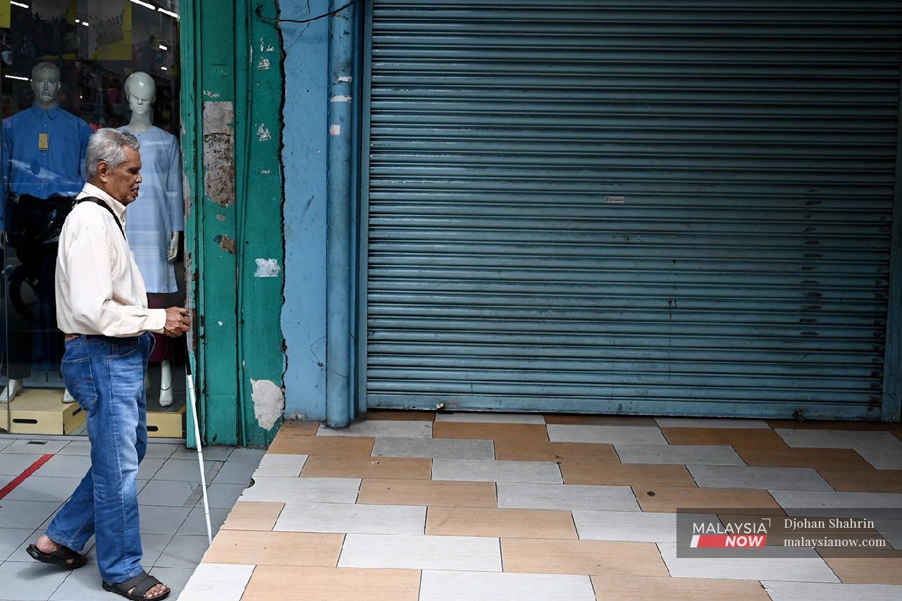Seorang lelaki OKU penglihatan, berjalan menggunakan tongkat di kawasan deretan kedai Jalan Chow Kit. Vaksinasi olongan itu perlu dipergiatkan dengan membantu mereka untuk mendaftarkan diri sebagai penerima vaksin.