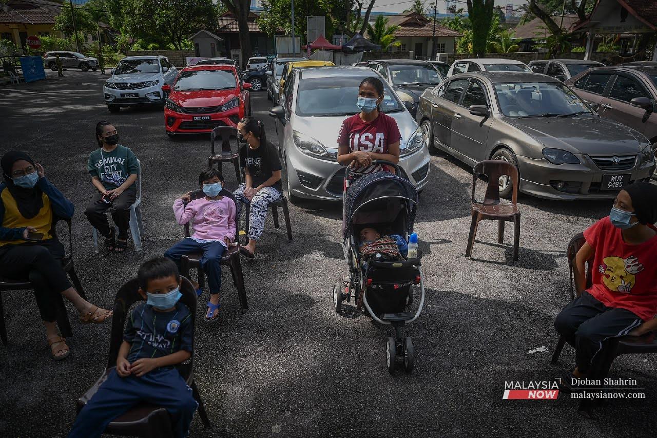 Orang Asli Temuan bersama anak-anak duduk menunggu giliran sebelum melakukan ujian saringan RTK-Antigen secara percuma oleh pasukan kesihatan.