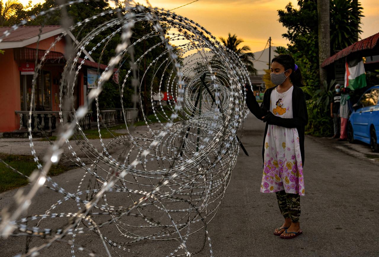 A girl in Kampung Dato’ Ahmad Said Tambahan 2 in Ipoh, Perak, looks at the barbed wire fence put up around the area which has been placed under enhanced movement control order until June 19. Photo: Bernama
