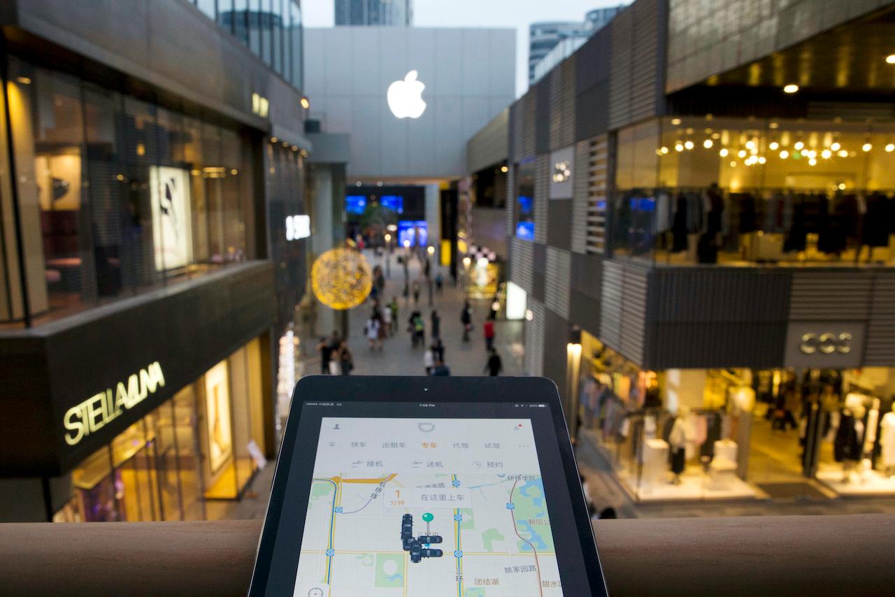 A mobile device displaying the Didi Chuxing app is held up near the Apple store logo in Beijing, China, May 13, 2016. Apple Inc had invested US$1 billion in the Chinese ride-hailing service, the main competitor in China for Uber Technologies Ltd. Photo: AP