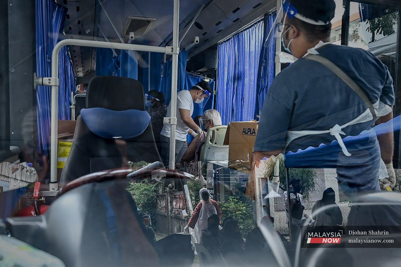 Health workers administer a dose of Covid-19 vaccine to a senior citizen in a bus repurposed as a mobile vaccination centre at the PKNS flats in Kampung Baru, Kuala Lumpur.