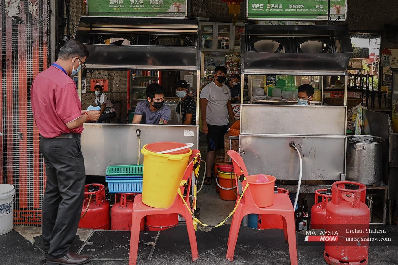 A customer waits for his food in front of a coffee shop at Jalan Tun Sambathan in Kuala Lumpur. Under the lockdown SOPs, only drive-thru, takeaway and food deliveries are allowed.