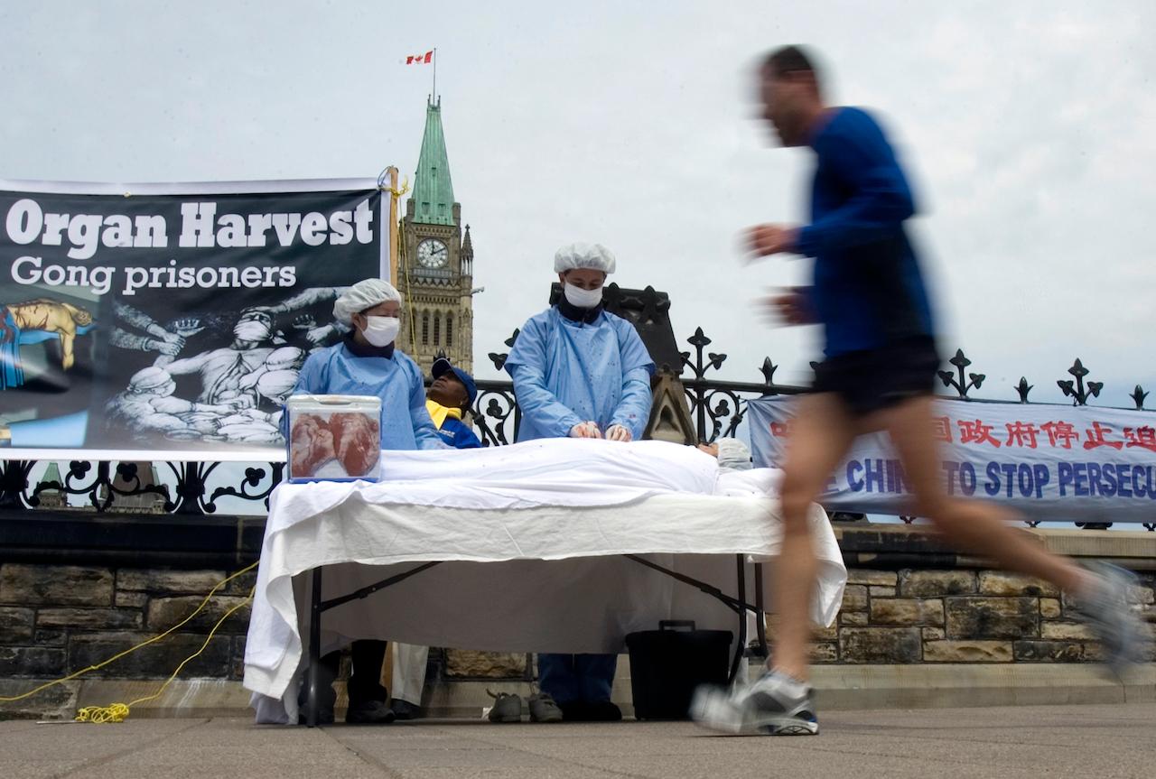 A man jogs past Falun Gong practitioners using a mock organ harvesting display as part of their protest against China and its persecution of Falun Gong practitioners, on Parliament Hill in Ottawa, May 2, 2008. The protesters claim that China illegally harvests organs from Falun Gong prisoners. Photo: AP