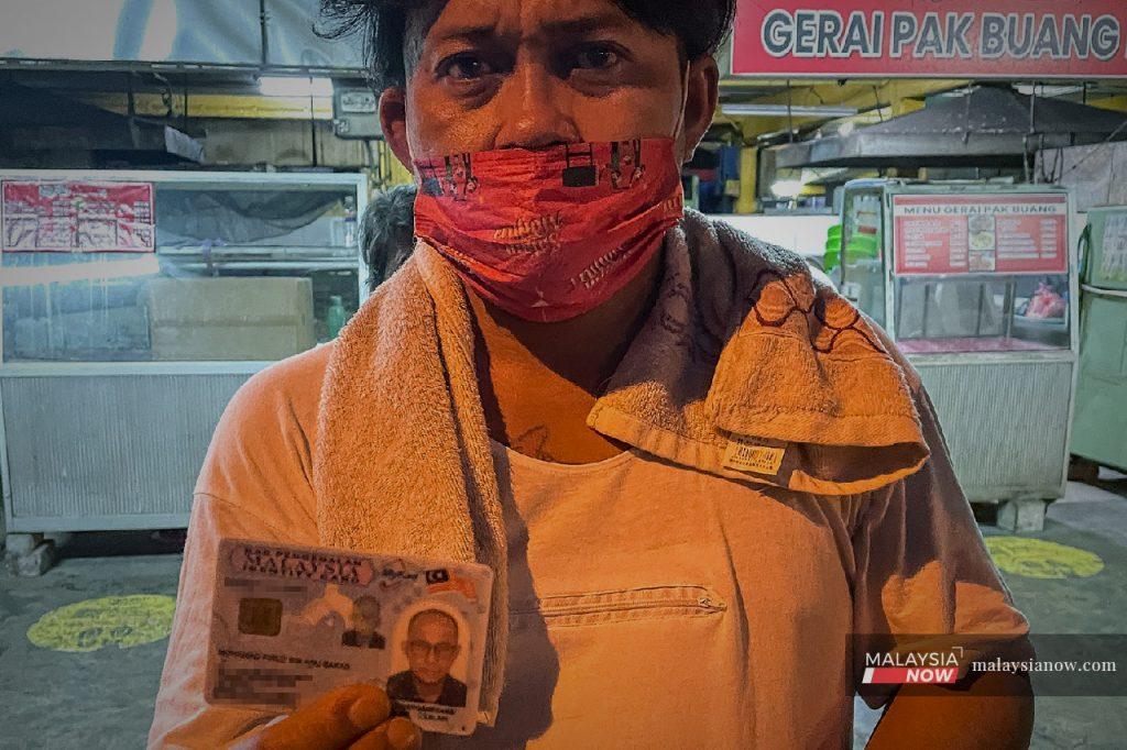 Mohd Firuz Abu Bakar menunjukkan kad pengenalannya di pasar terbuka di Kuching, tempat dia berteduh pada waktu malam. Di memiliki MyKad, namun tidak tahu bagaimana mendaftar diri bagi mendapatkan vaksin.