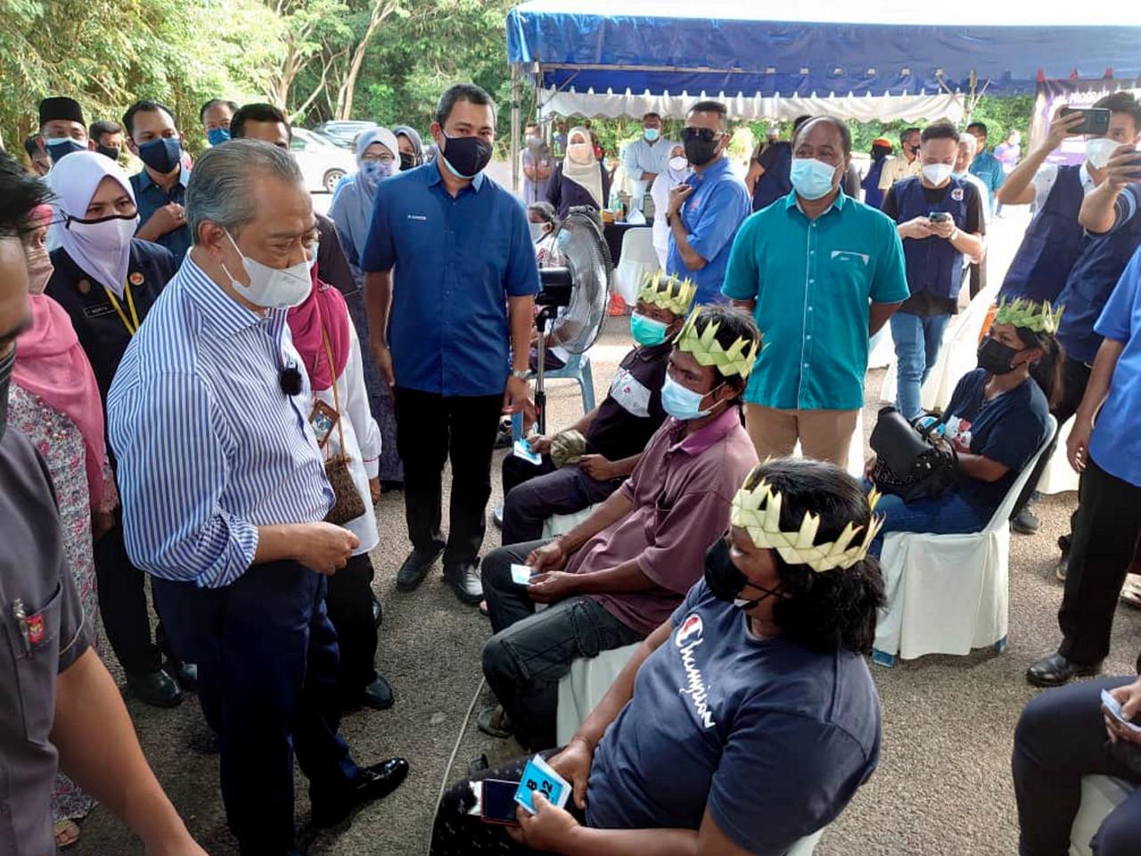 Prime Minister Muhyiddin Yassin speaks to a group of Orang Asli awaiting their turn for vaccination at the Pagoh multipurpose hall in Muar yesterday. Photo: Bernama