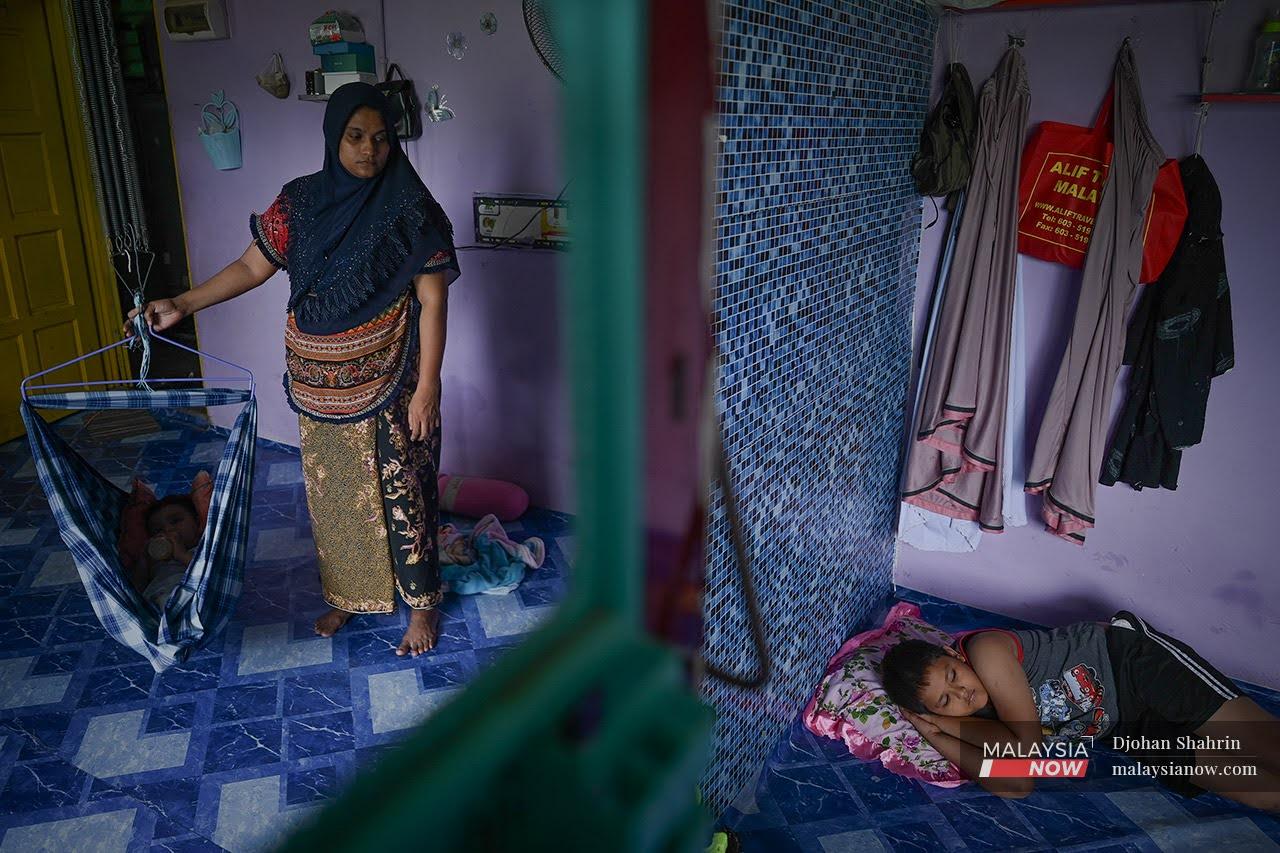 A Rohingya woman rocks a baby with one hand as she watches over another child in a house in Selayang, Kuala Lumpur.