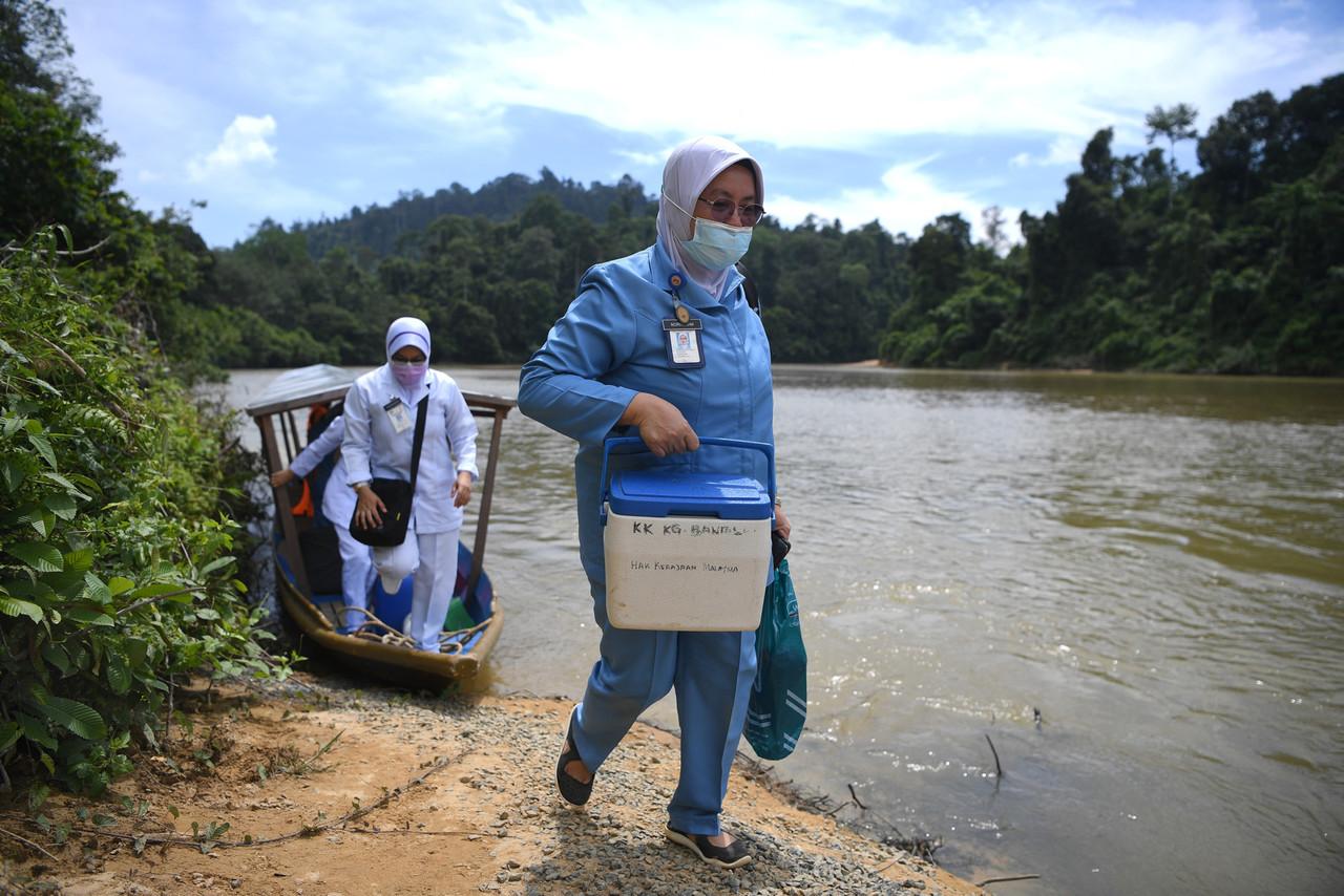 Health workers carrying vaccination equipment disembark from a boat in Jerantut, Pahang, to vaccinate members of the Orang Asli community in Kampung Orang Asli Sungai Kucing. Photo: Bernama